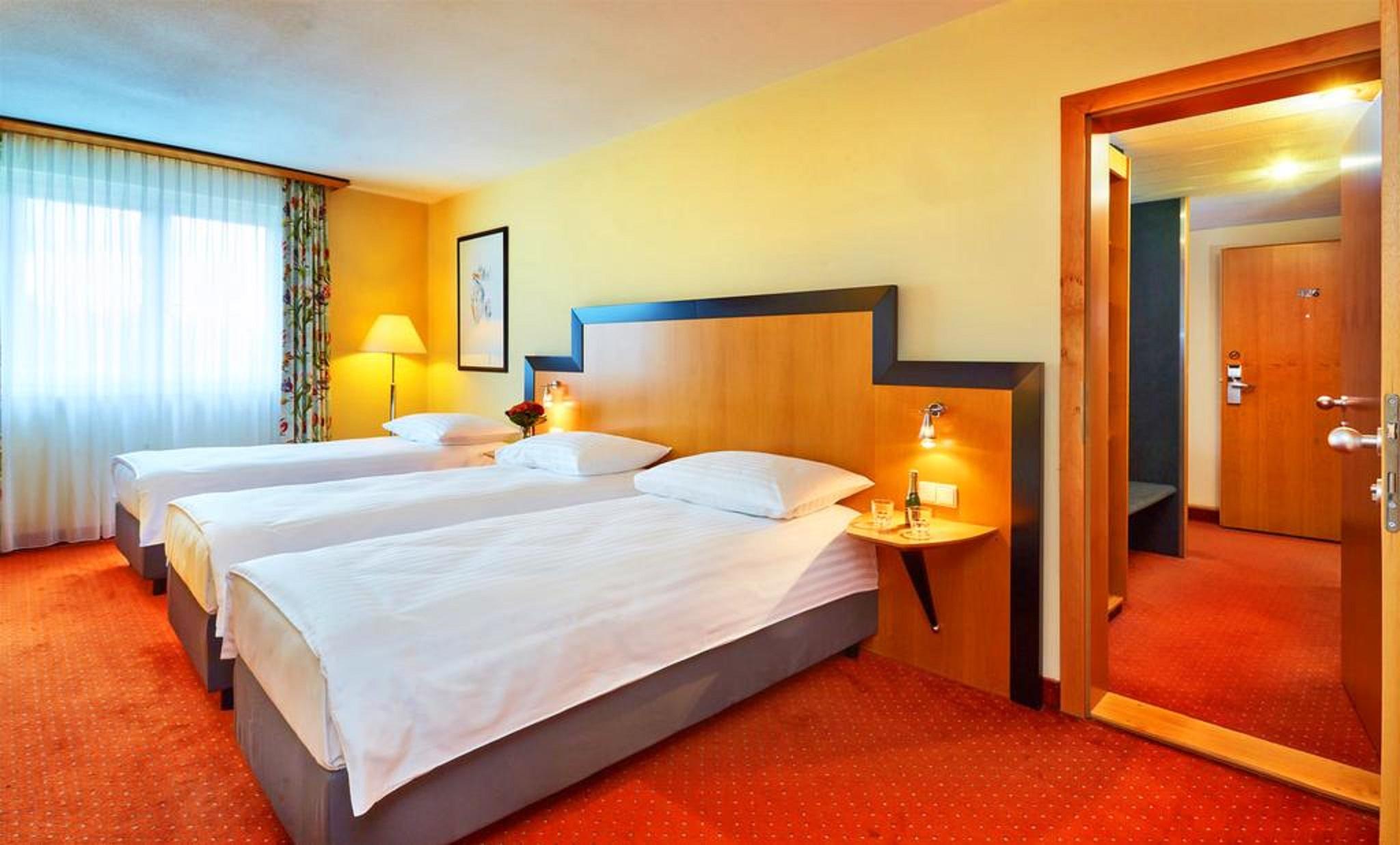 Don Giovanni Hotel Prague - Great Hotels Of The World Exterior photo The photo shows a brightly lit hotel room featuring three single beds with white bedding and gray bases. The walls are painted a warm yellow, and there are decorative curtains on the window, allowing natural light to enter. A bedside table is next to