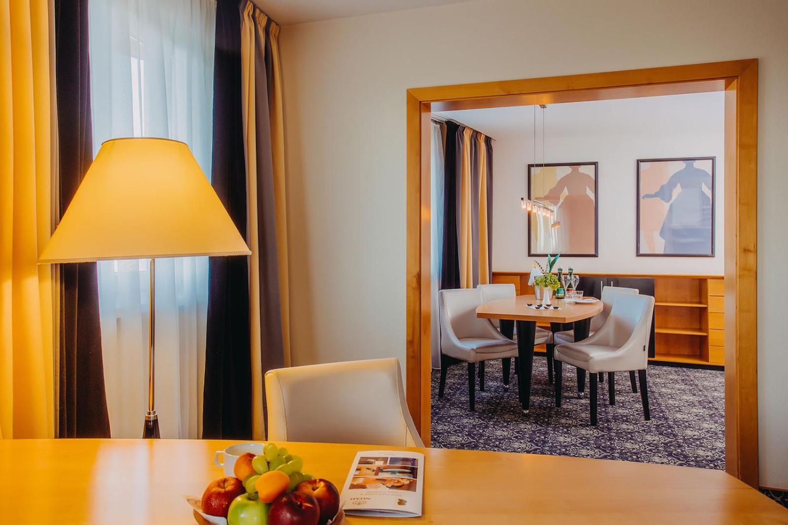 Don Giovanni Hotel Prague - Great Hotels Of The World Exterior photo The photo shows a well-decorated interior space, likely a hotel room or a suite. In the foreground, there is a wooden table with a bowl of colorful fruits and a magazine resting on the surface. A modern lamp stands beside the table, providing soft li